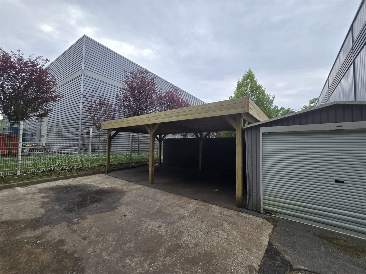 Abri en bois à toit plat installé près d’un bâtiment professionnel.