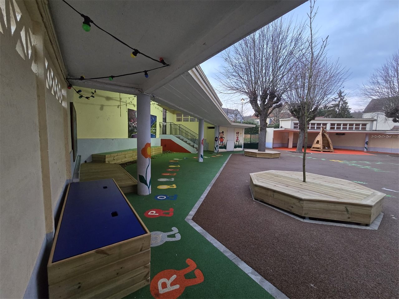 Cour d’établissement avec bancs autour des arbres, rangements et aménagements en bois.