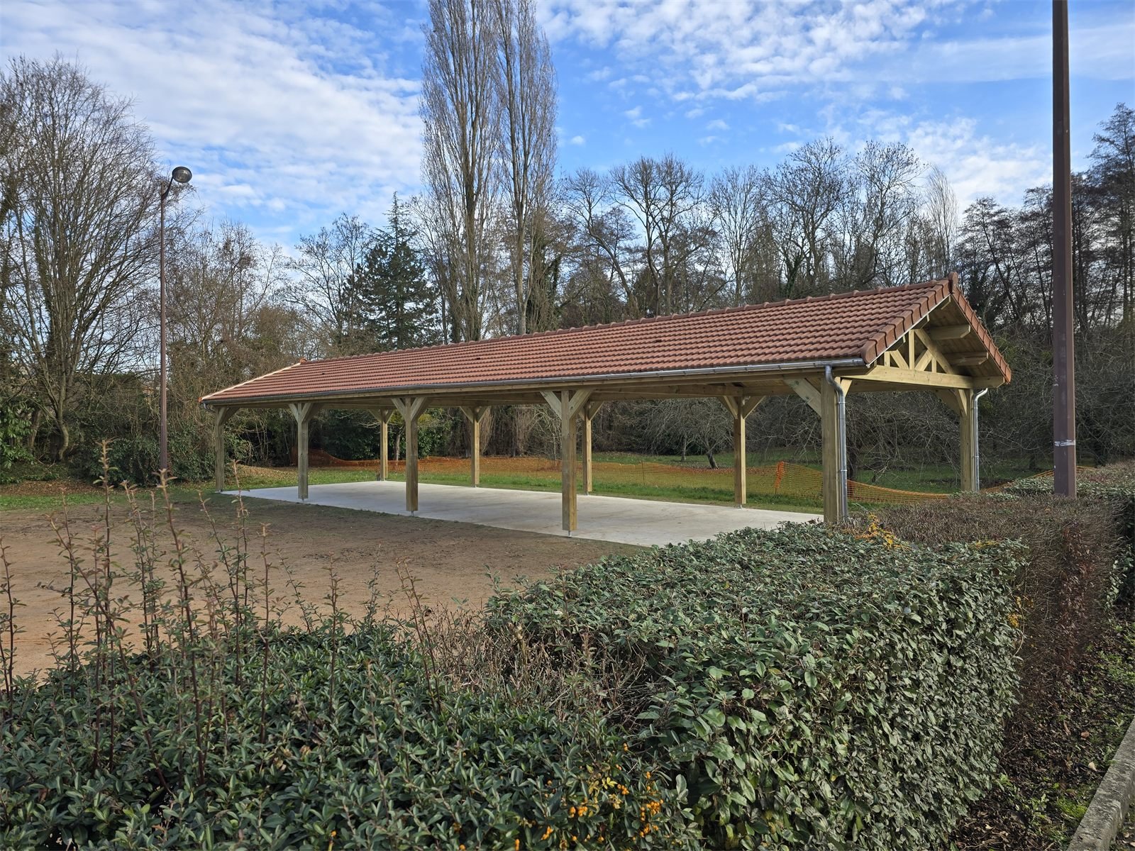Grand préau en charpente bois avec couverture en tuiles et dalle béton.